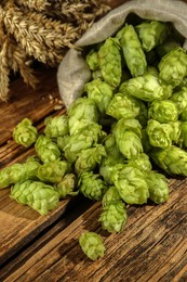 Overturned sack of hop flowers and wheat ears on wooden table, closeup