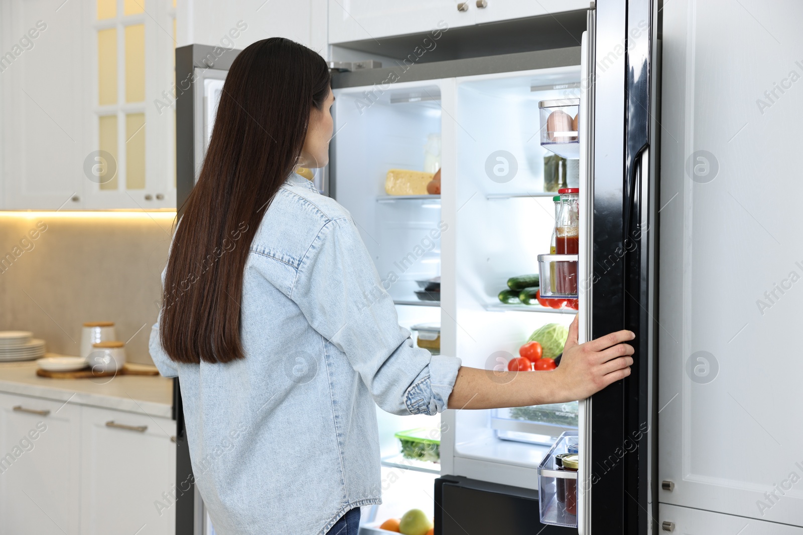 Photo of Young woman near modern refrigerator in kitchen