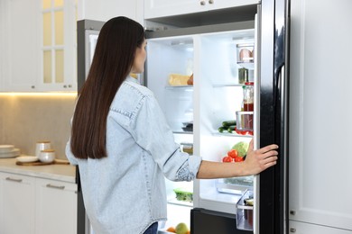 Young woman near modern refrigerator in kitchen