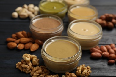 Jars with butters made of different nuts and ingredients on black wooden table, closeup