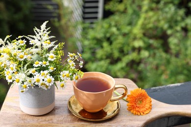 Photo of Cup of delicious chamomile tea and fresh flowers outdoors on sunny day. Space for text