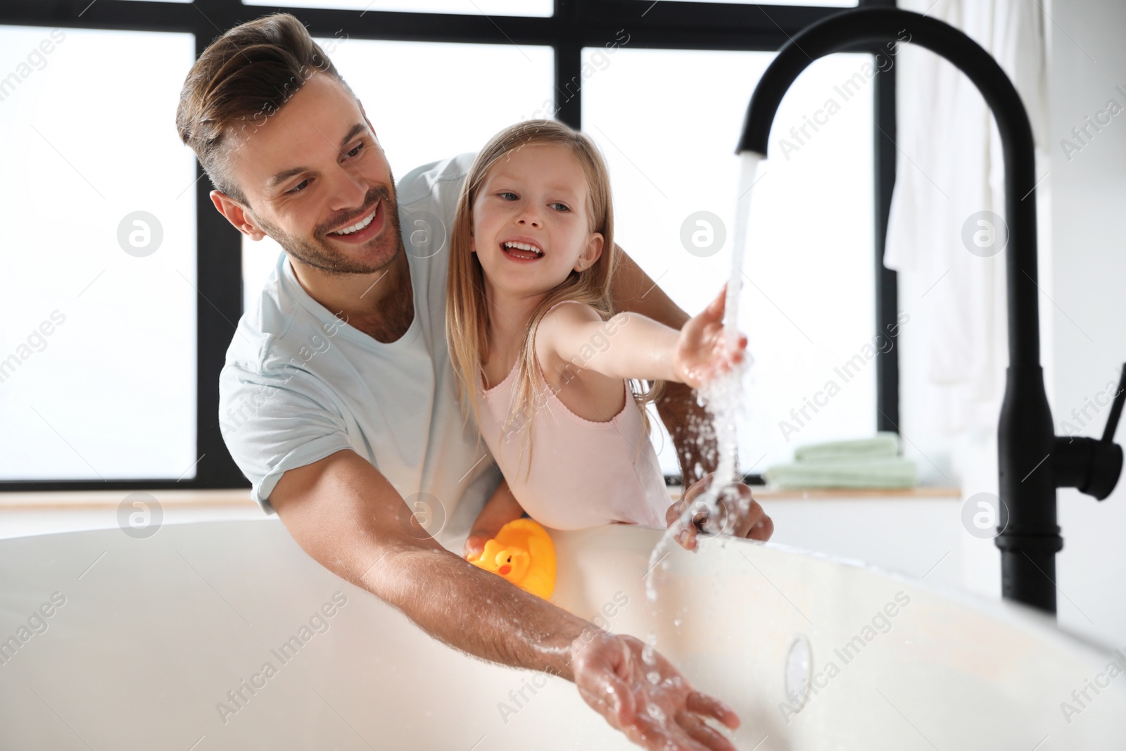 Photo of Father with his cute little daughter filling tub in bathroom