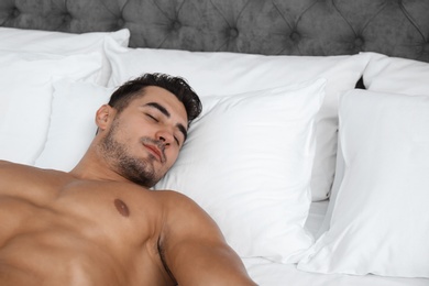 Photo of Sexy young man sleeping on bed with soft pillows at home