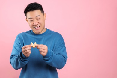 Photo of Happy asian man holding tasty fortune cookie with prediction on pink background. Space for text