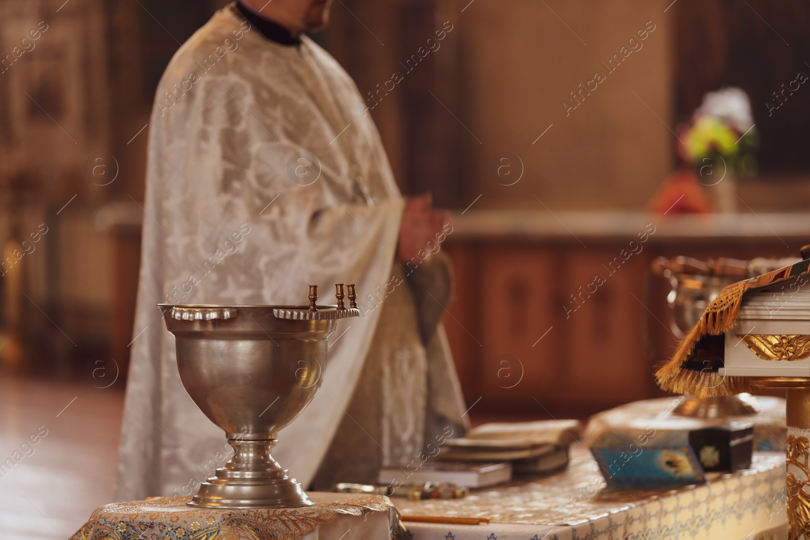 Photo of MYKOLAIV, UKRAINE - FEBRUARY 27, 2021: Priest conducting baptism ceremony in Kasperovskaya icon of Mother of God cathedral, focus on vessel with holy water