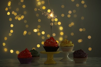 Different colorful cupcakes and one with sparkler on table against blurred lights