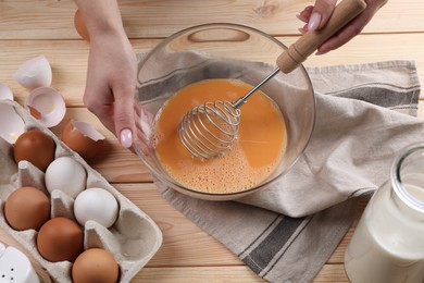 Photo of Woman whisking eggs in bowl at wooden table, above view