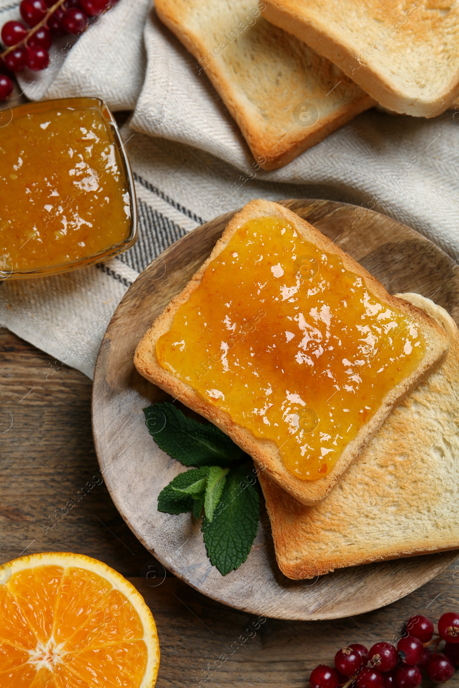 Photo of Delicious toasts served with jam, orange and berries on wooden table, flat lay