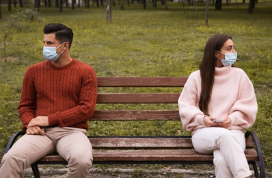 Photo of Man and woman sitting on bench in park. Keeping social distance during coronavirus pandemic
