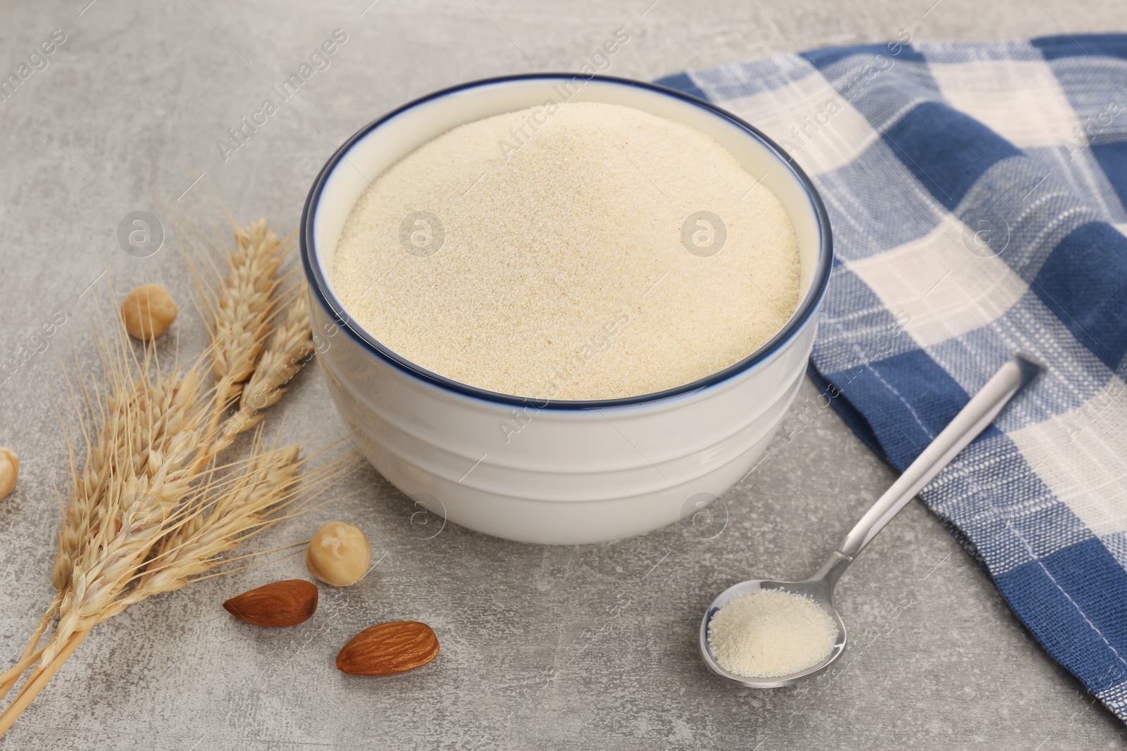 Photo of Uncooked organic semolina, spikelets and different nuts on grey table