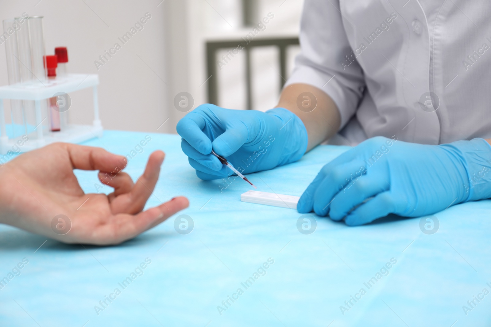 Photo of Doctor testing blood sample from patient's finger at table in clinic, closeup