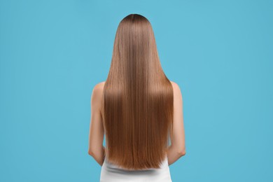 Woman with healthy hair on light blue background, back view