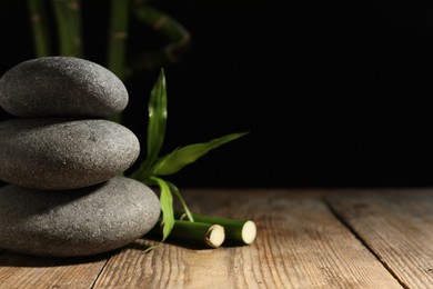 Photo of Spa stones and bamboo stems on wooden table against dark background, space for text