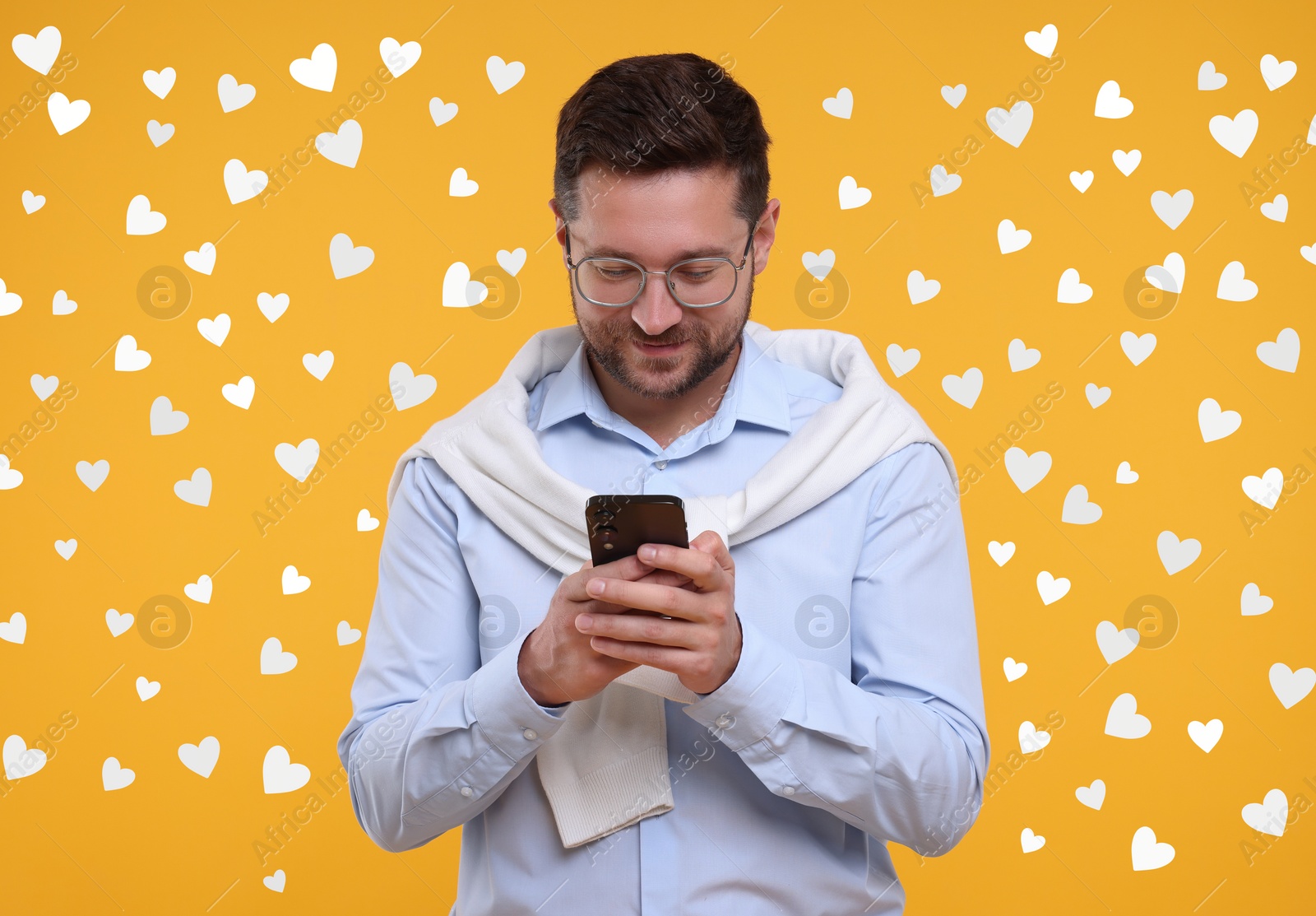 Image of Long distance love. Man chatting with sweetheart via smartphone on golden background. Hearts around him