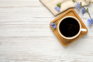 Cup of delicious chicory drink and flowers on white wooden table, flat lay. Space for text