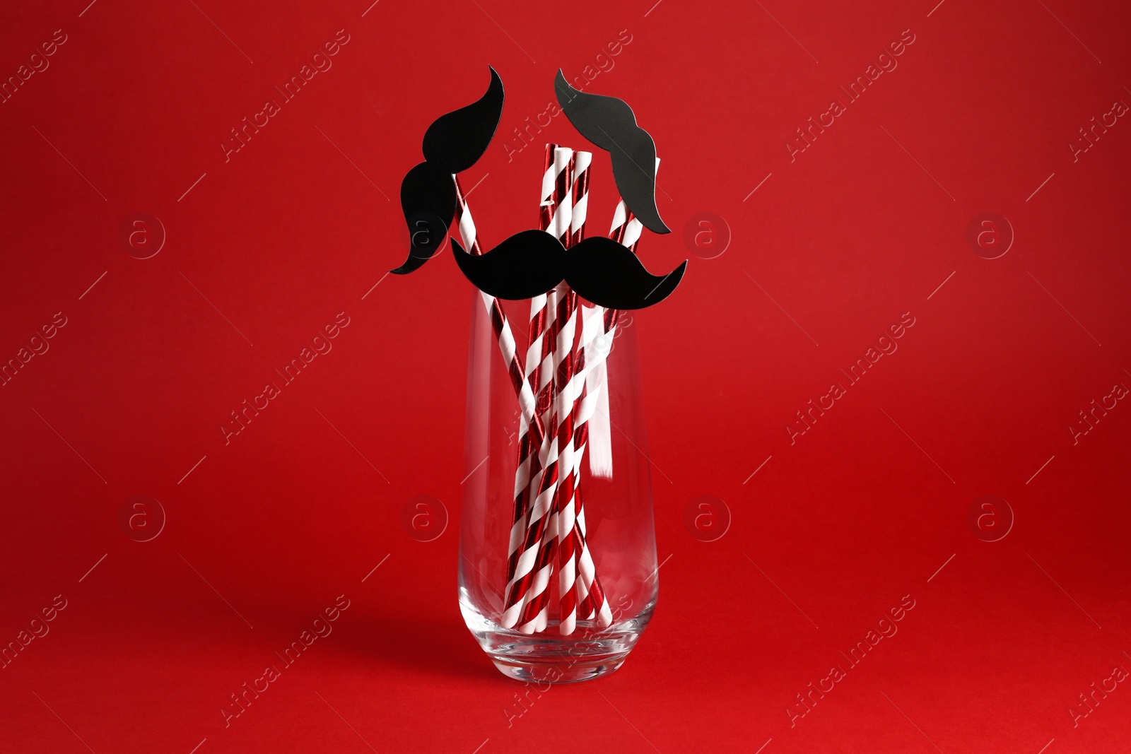 Photo of Fake paper mustaches and party props in glass on red background