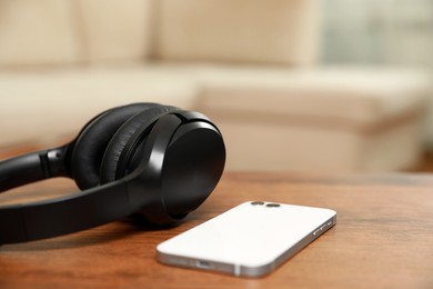 Photo of Modern wireless headphones and smartphone on wooden table indoors, closeup