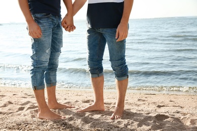 Gay couple standing barefoot on beach, closeup