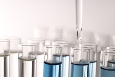 Photo of Dripping liquid from pipette into test tube on light background, closeup