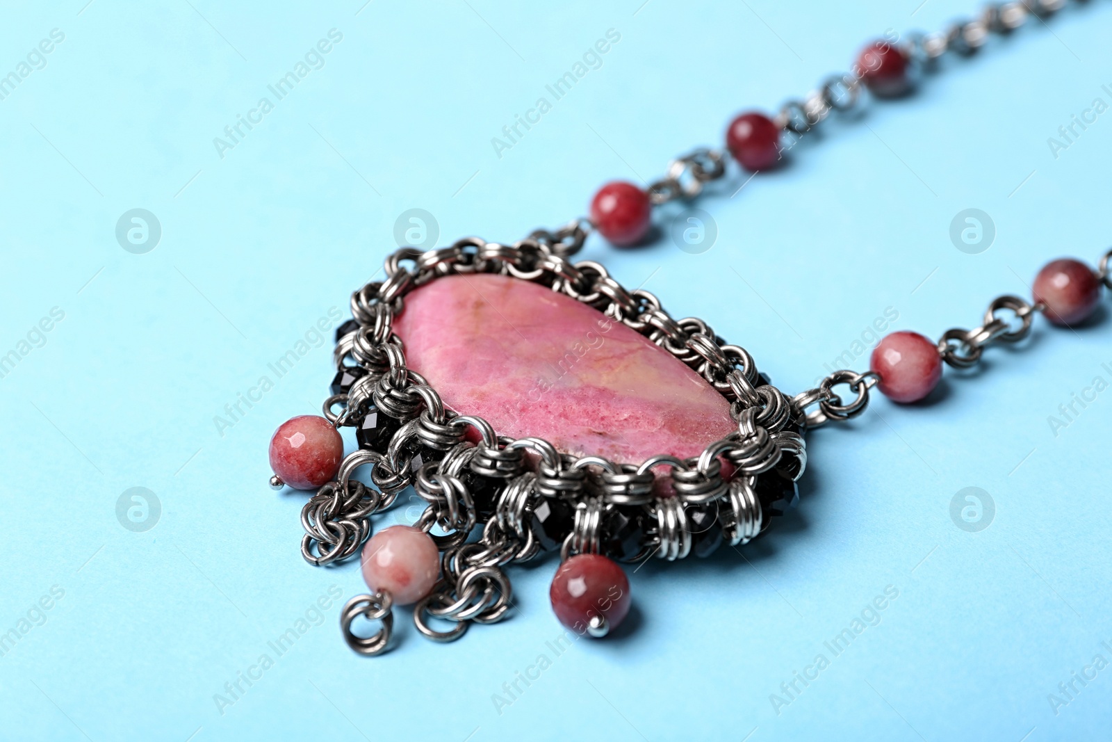 Photo of Beautiful silver necklace with rhodonite and tourmaline gemstones on light blue background, closeup