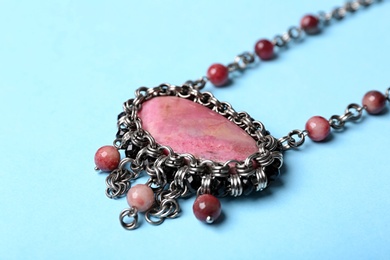 Photo of Beautiful silver necklace with rhodonite and tourmaline gemstones on light blue background, closeup