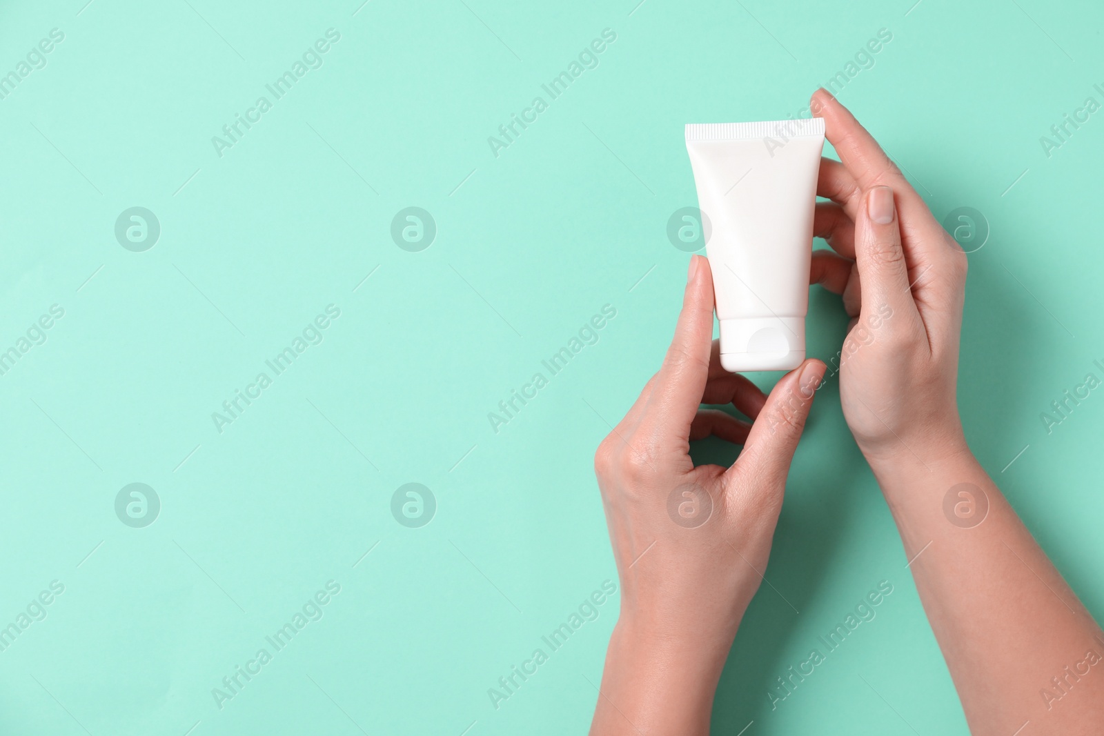 Photo of Woman with tube of hand cream on turquoise background, top view. Space for text