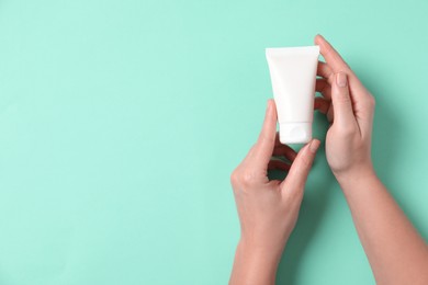 Photo of Woman with tube of hand cream on turquoise background, top view. Space for text