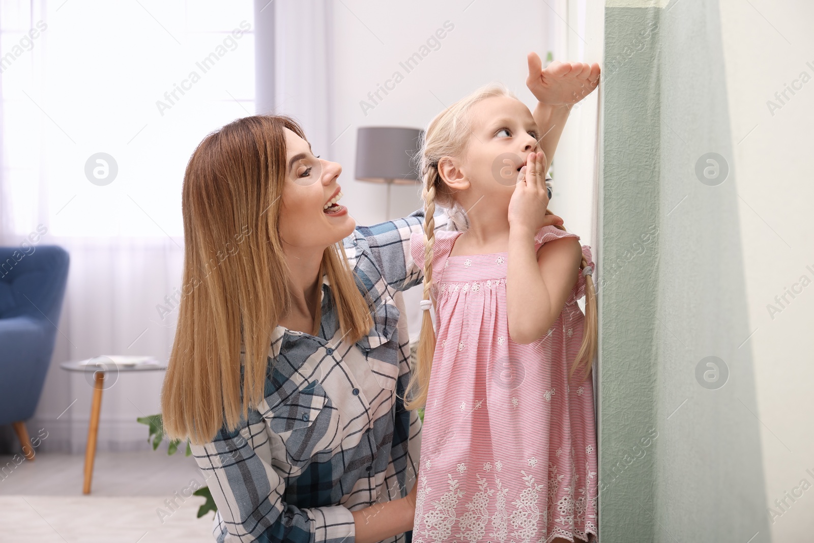 Photo of Young woman measuring her daughter's height at home