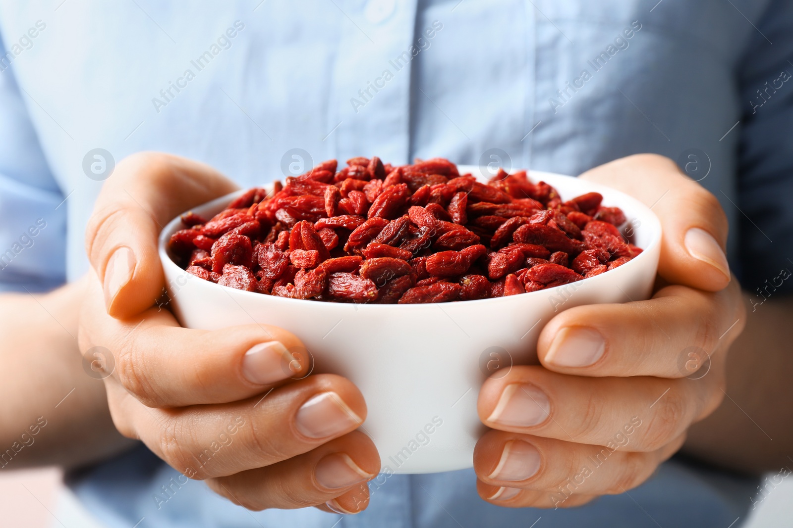 Photo of Woman holding bowl of red dried goji berries, closeup