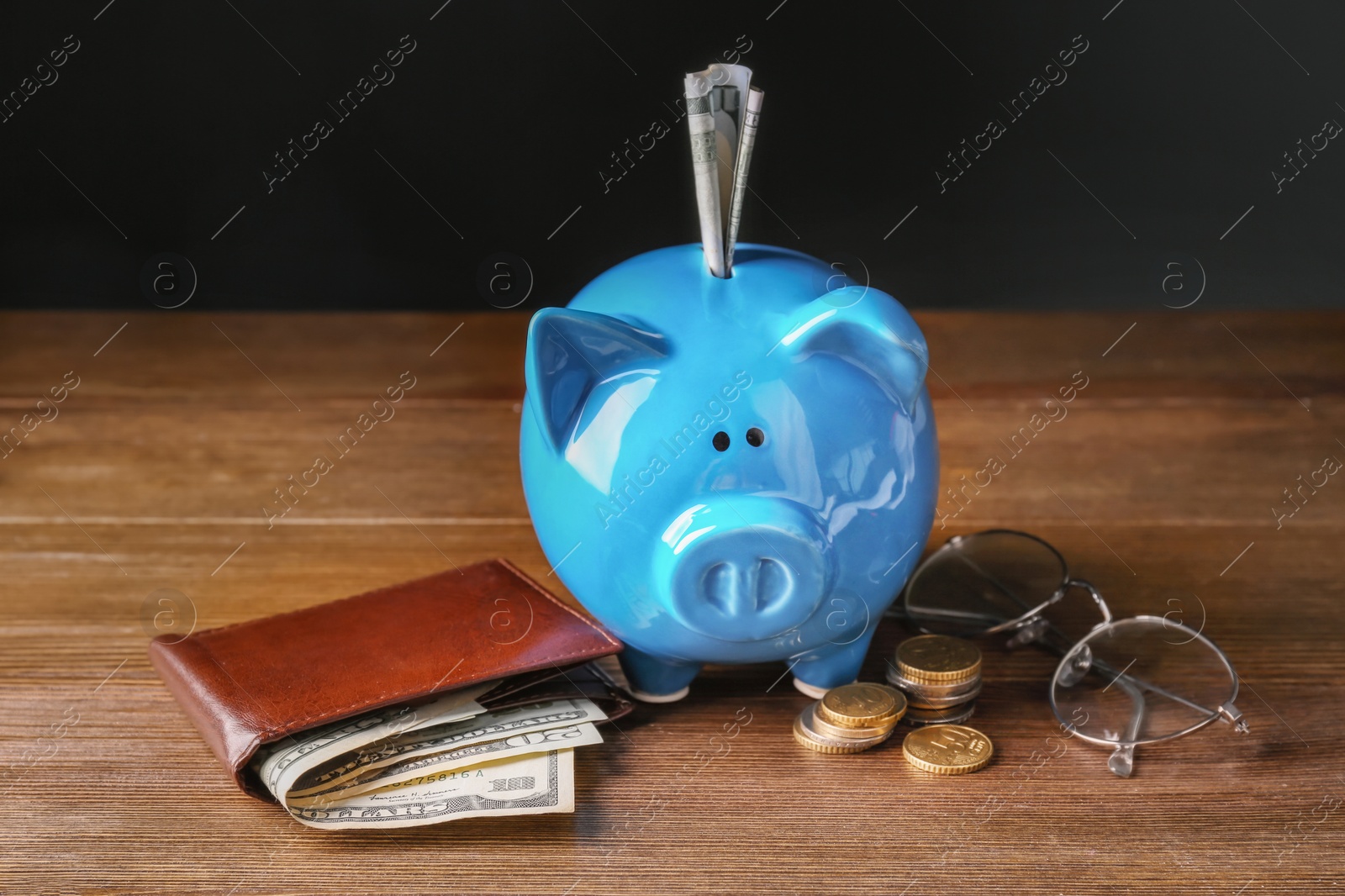Photo of Piggy bank with banknotes, wallet and eyeglasses on wooden table. Pension planning