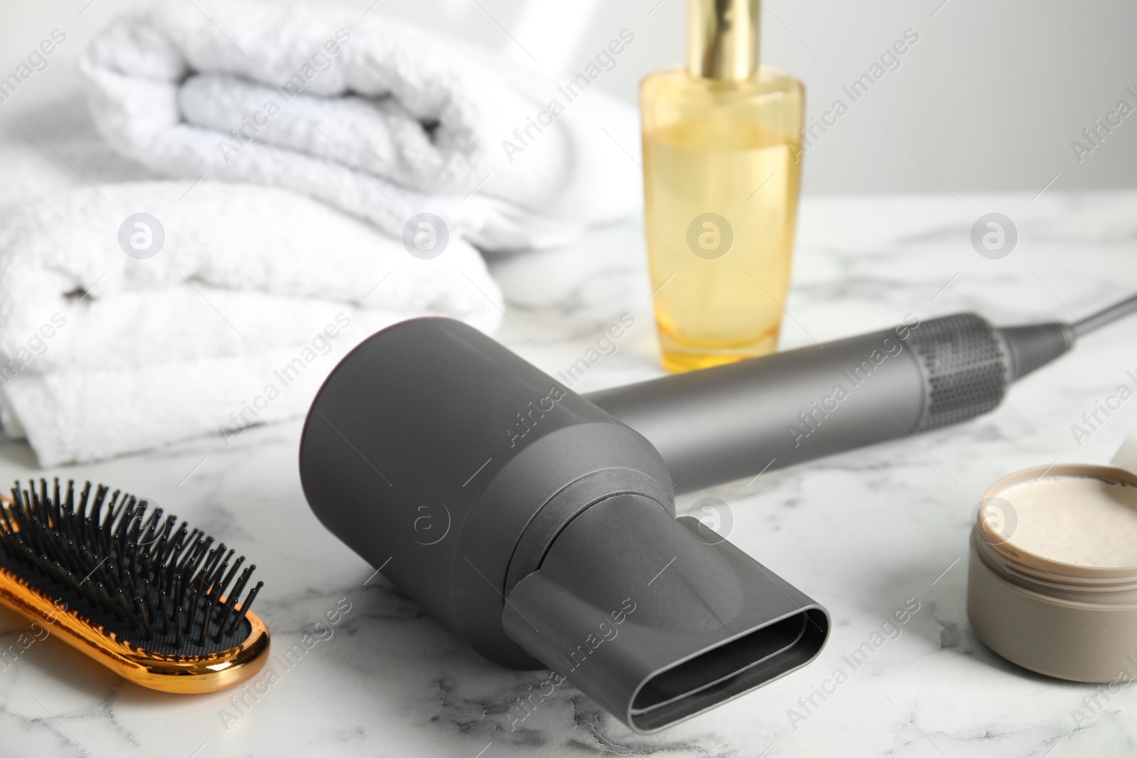 Photo of Hair care products, dryer and brush on white marble table