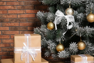 Photo of Decorated Christmas tree and gift boxes near brick wall, closeup