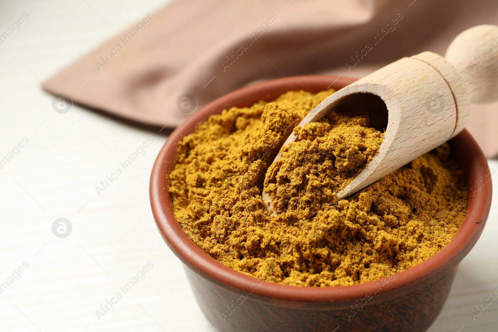 Photo of Curry powder in bowl and scoop on white table, closeup