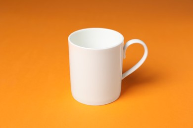 Photo of One white ceramic mug on orange background