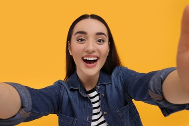 Photo of Smiling young woman taking selfie on yellow background