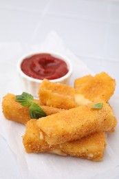 Tasty fried mozzarella sticks with basil leaves and ketchup on white table, closeup