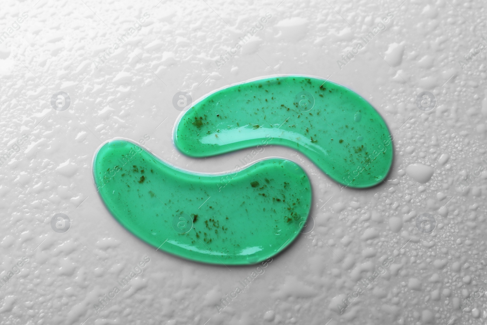 Photo of Green under eye patches on light grey wet background, flat lay. Cosmetic product
