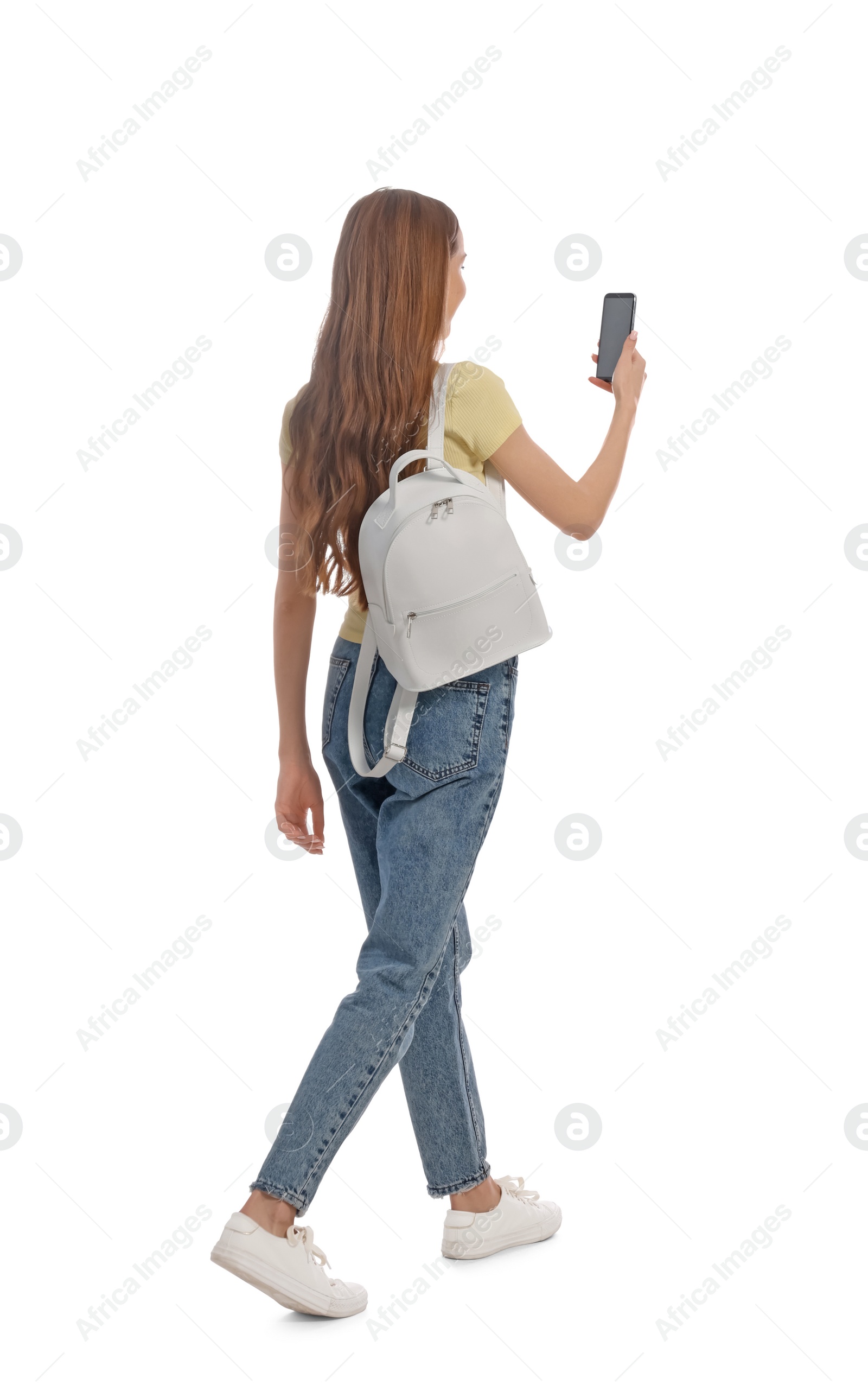 Photo of Young woman in casual outfit using smartphone while walking on white background