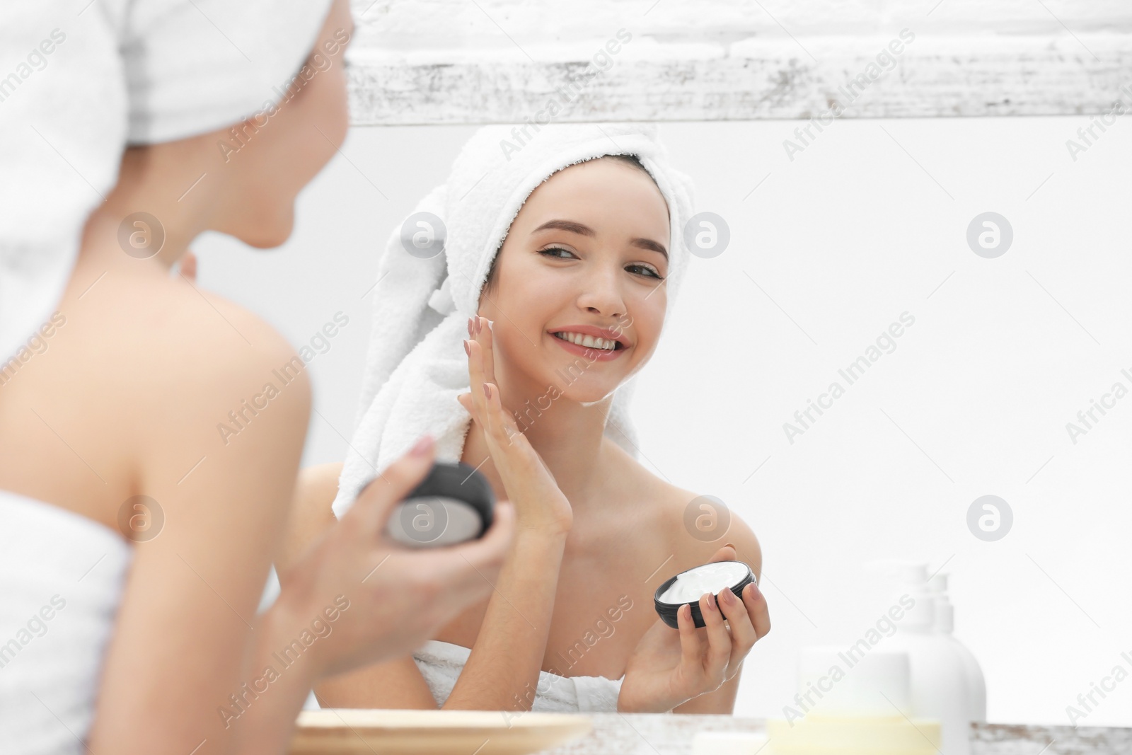 Photo of Teenage girl with acne problem using cream while looking in mirror indoors