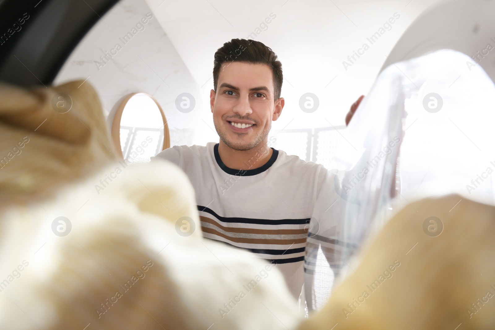 Photo of Man putting clothes into washing machine in bathroom, view from inside. Laundry day