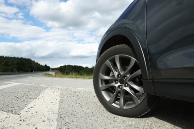 Photo of New black modern car on asphalt road, closeup. Space for text