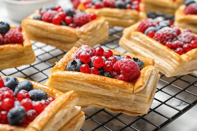 Cooling rack and fresh delicious puff pastry with sweet berries on white marble table, closeup