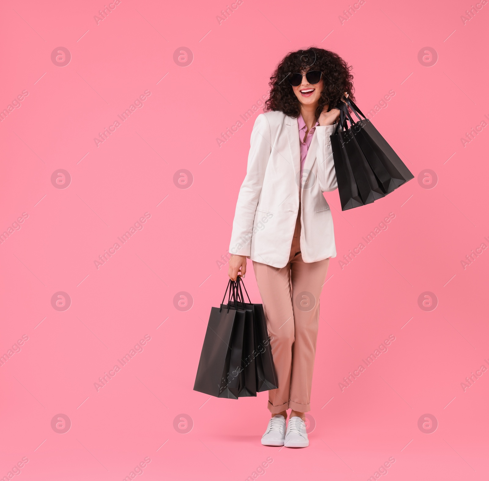 Photo of Happy young woman with shopping bags and stylish sunglasses on pink background. Space for text