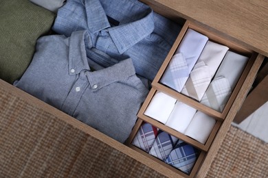 Photo of Open drawer with folded handkerchiefs and clothes indoors, top view