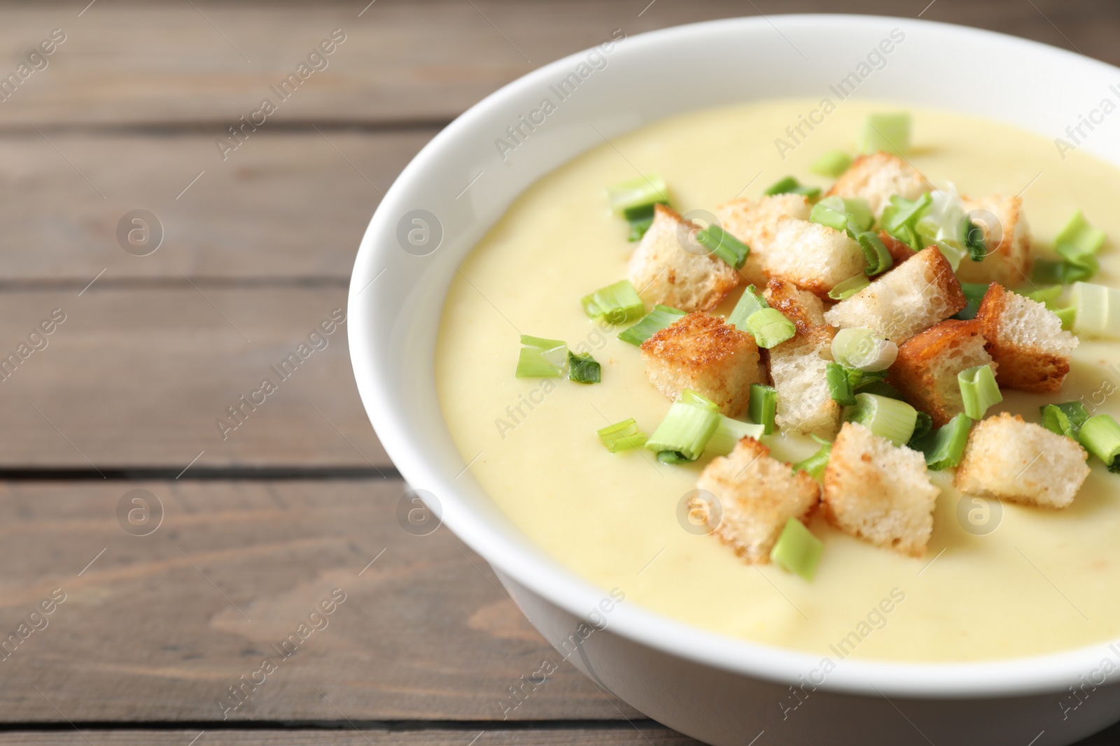 Photo of Tasty potato soup with croutons and green onion in bowl on wooden table, closeup. Space for text