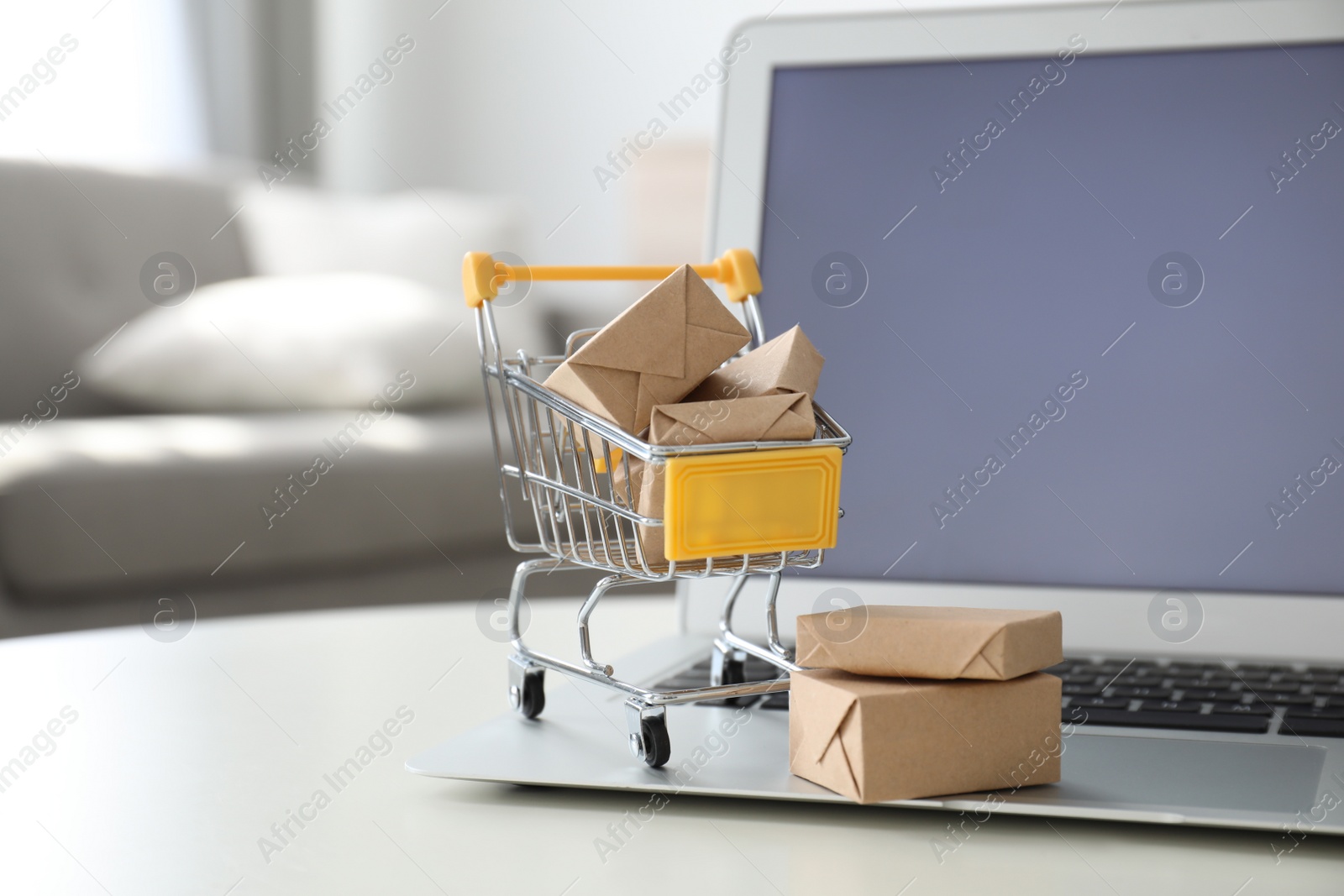 Photo of Internet shopping. Laptop and small cart with boxes on table indoors