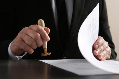 Photo of Male notary stamping document at table, closeup