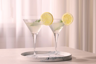 Photo of Marble tray with martini glasses of fresh cocktail, rosemary and lemon slices on beige table indoors