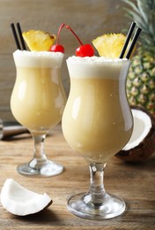 Photo of Tasty Pina Colada cocktail and ingredients on wooden table