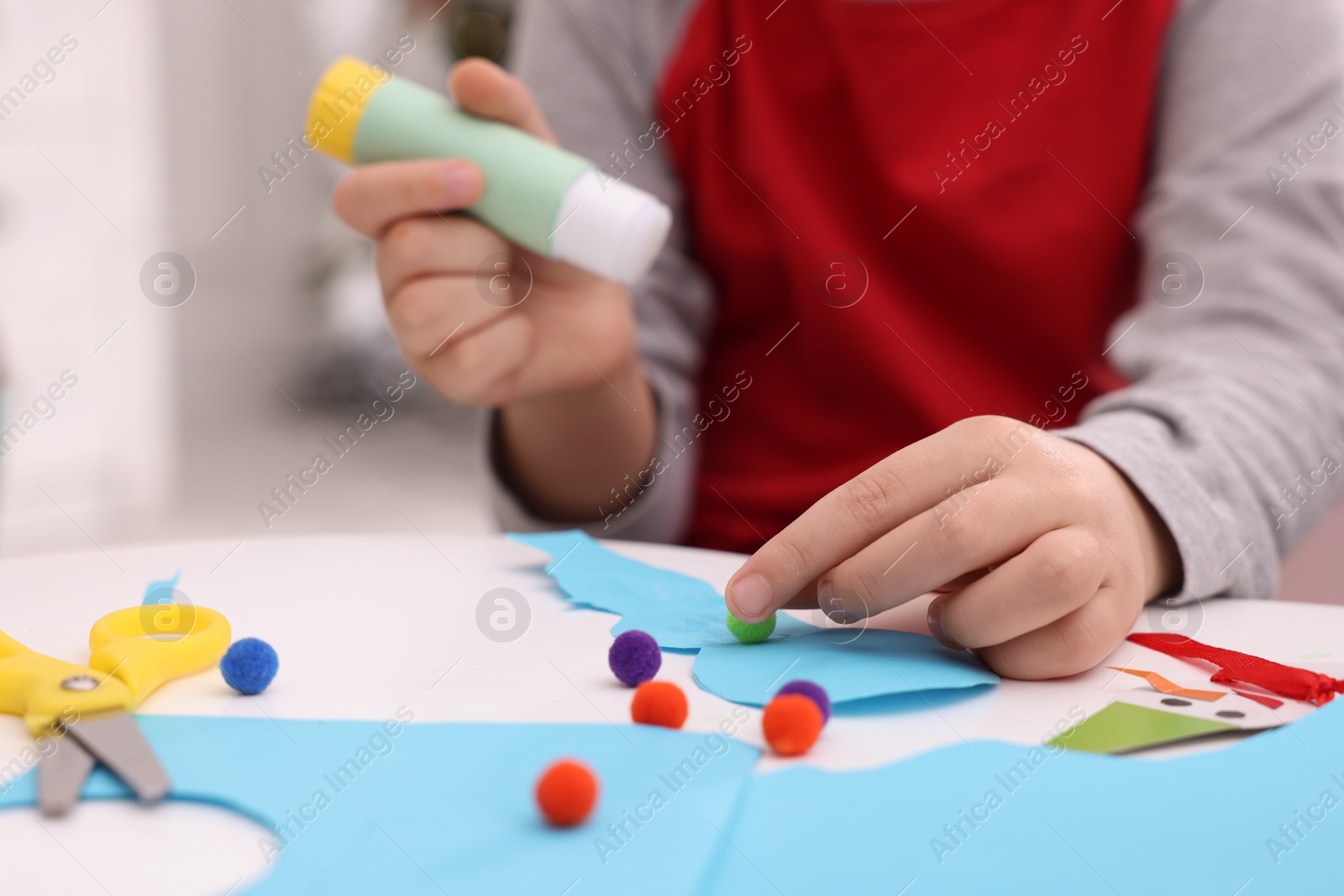 Photo of Little child making Christmas craft at white table, closeup